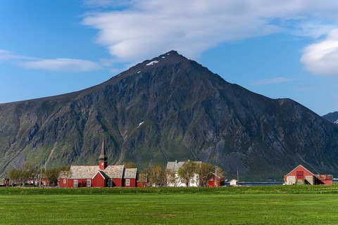 The small village of Flakstad with its red church and a few houses, with Mount Hustinden in the