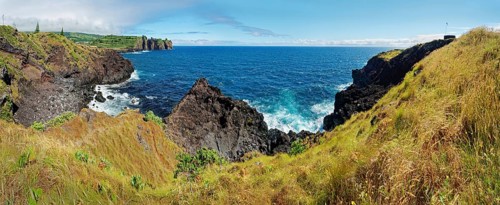 Panorama of a rocky coastal view with rugged cliffs plunging into the blue sea under a clear sky,