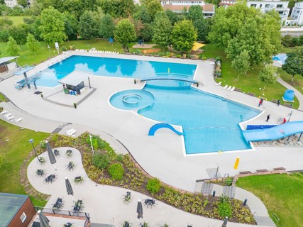 Aerial view of an outdoor pool with swimming pool, deckchairs and tables, surrounded by trees and
