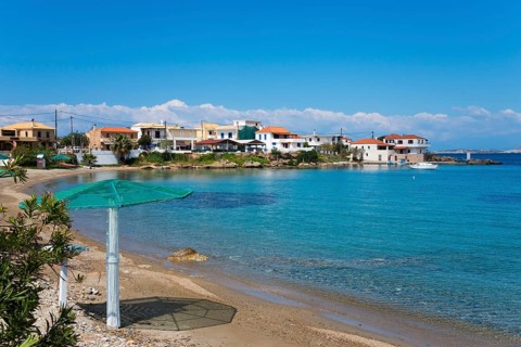 A quiet beach with clear water and houses on the shore under a blue sky, Archangelos, Mani,