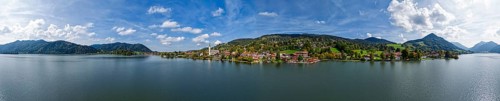 Painter's panoramic view of a Bavarian village on a lake, surrounded by mountains under a blue sky
