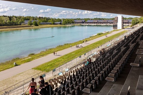 View from the grandstand of a lake with paddlers, surrounded by a natural landscape,
