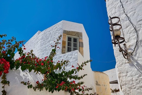 White building with flower tendrils and windows under a bright blue sky, Chora, Old Town, Patmos,