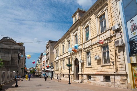 A lively city street with historic architecture and balloon decorations on a sunny day, pedestrian