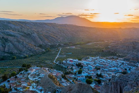 A village lies in a valley surrounded by hills and mountains as the sun sets and the valley glows