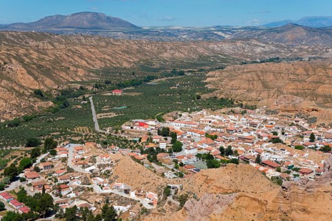 A small village with orange-coloured roofs is nestled in a green valley surrounded by mountains
