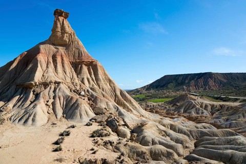 View of a rock formation in a dry, barren desert landscape. In the background, other hills rise up
