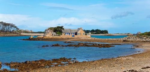 A stone house on a small island surrounded by calm water and rocks, house on the Plage de Raluzet,