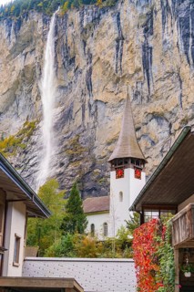 Church tower in front of a dramatic waterfall and rock face in an autumn landscape, Lauterbrunnen,