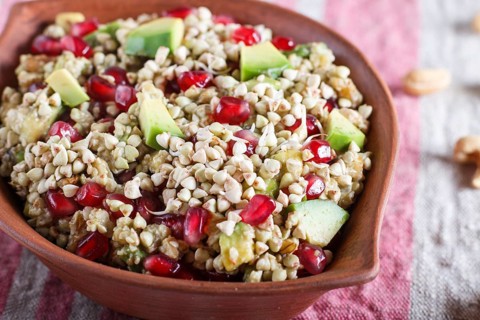 Salad of germinated buckwheat, avocado, walnut and pomegranate seeds in clay plate on white wooden