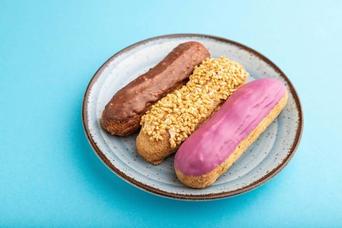 Set of eclair, traditional french dessert on ceramic plate on blue pastel background. side view,