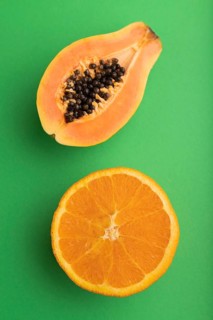Ripe cut papaya and orange on green pastel background. Top view, flat lay, close up. Tropical,