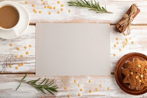 Gray paper sheet mockup with cup of coffee and cake on white wooden background. Blank, top view,