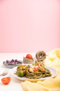 Tagliatelle green spinach pasta with tomato, pea and microgreen sprouts on a white and pink