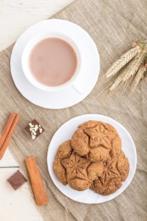 Homemade oatmeal cookies with a cup of cocoa on a linen textile and white wooden background. top