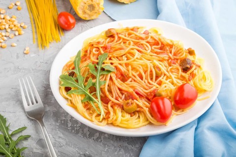 Corn noodles with tomato sauce and arugula on a gray concrete background and blue textile. Side