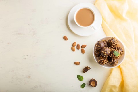 Chocolate caramel ball candies with almonds and a cup of coffee on a white wooden background and