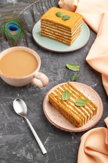 Homemade honey cake with milk cream and mint with cup of coffee on a black concrete background and