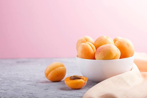 Fresh orange apricots in white bowl on gray and pink pastel background. side view, copy space,