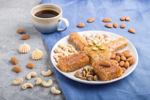 Traditional arabic sweets (basbus, kunafa, baklava), a cup of coffee and nuts on a gray concrete