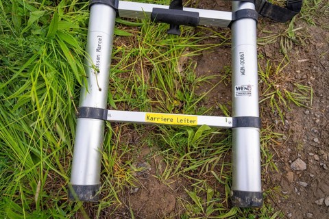 A metal ladder lies on a grass- and dirt-covered ground surface, fibreglass installation, Calw