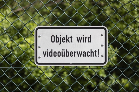 Sign mounted on a green wire mesh fence with the inscription: Objekt wird videoüberwacht! in