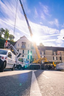 A lifting crane and construction workers during construction work on a sunny street in front of