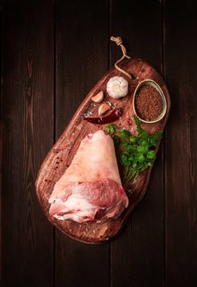 Raw pork knuckle, on a wooden chopping board, with spices, close-up, top view, no people