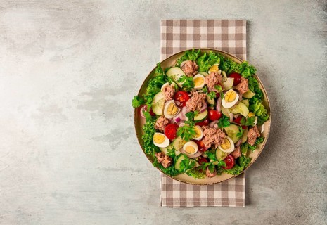 Tuna salad, vegetable salad with quail eggs, lettuce, red onion and cucumbers, on a light gray
