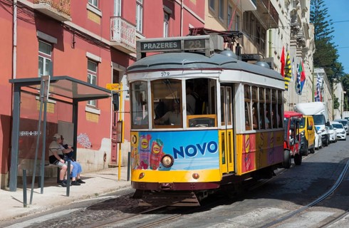 A yellow-purple tram with Novo advertising runs along the street with people in the background,
