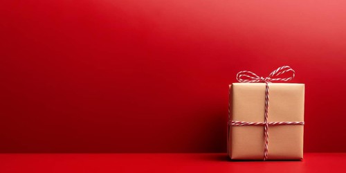 Banner with small Christmas gift box wrapped in kraft paper on red background with copy space.