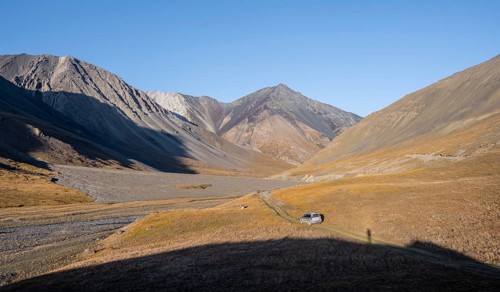Off-road vehicle on a track in the Burkhan valley, mountain landscape with golden meadows, Terskey