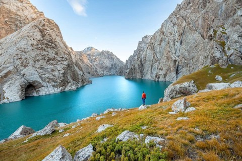 Young man at the turquoise mountain lake Kol Suu with rocky steep mountains, Kol Suu Lake, Sary