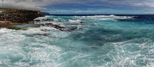 Stormy waves crash against a rocky shore under a cloudy sky, seawater bathing establishment,