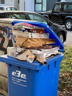 Overflowing waste paper bin, standing on a pavement, waiting to be emptied by a municipal waste