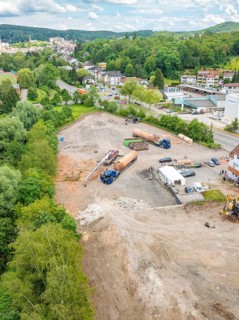 Large-scale aerial view of a construction site with machines, surrounded by trees and buildings,