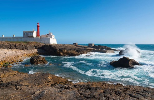 Lighthouse on the coast with rough waves and rocks under a blue sky, Farol do Cabo Raso, São Brás
