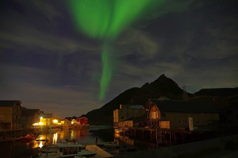 Glowing green aurora borealis over a fjord with houses and mountains at night, winter, Nyksund,