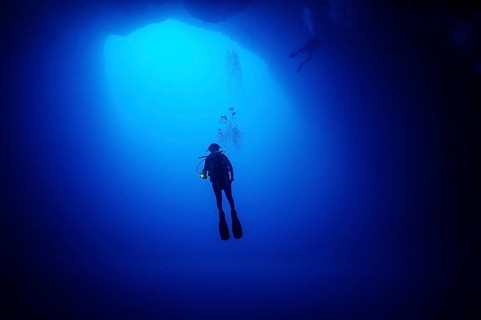 Female diver scuba diver diving in floating under opening cave opening large hole in seabed