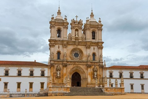 Majestic Gothic monastery façade with ornate towers against a cloudy sky, Mosteiro de Alcobaça,