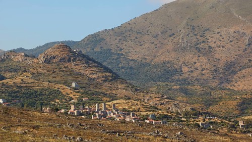 View of a quiet rural village surrounded by mountainous landscape under a clear blue sky,
