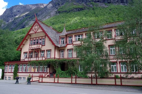 Historic Victorian-style building surrounded by green mountains and trees with striking red