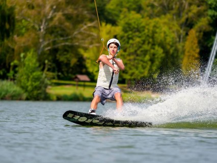 Young man on wakeboard in splashing water, cheerful, water skiing and wakepark, water sports