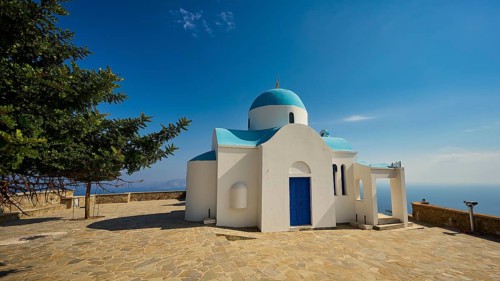 White-blue church with a tree next to it under a blue sky, Church of Profitis Ilias, above Nikia,