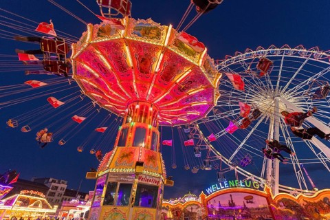 A funfair at dusk with illuminated chain carousel and Ferris wheel, Europa Rad, rides, wave flight,