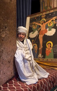 Ethiopian Orthodox priest in front of an image of the crucifixion of Jesus in the rock church of
