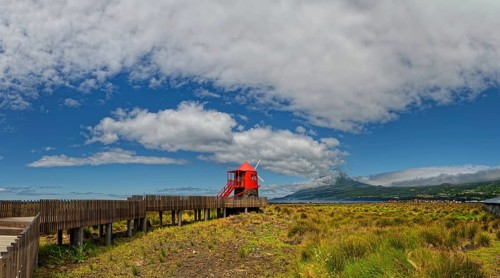 Wooden path leads to the Moinho das Lajes windmill with a dramatic sky and the volcanic cone of