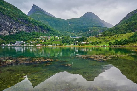 Mountainous landscape with a calm fjord reflecting the surrounding mountains and village,