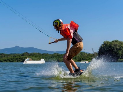 Young casual man with flapping shirt on wakeboard jumping into the lake, water ski and wakepark,
