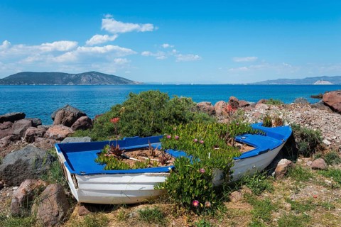 Old boat filled with plants on a rocky shore with sea view and flowers, Agíos Nikólaos, Agios